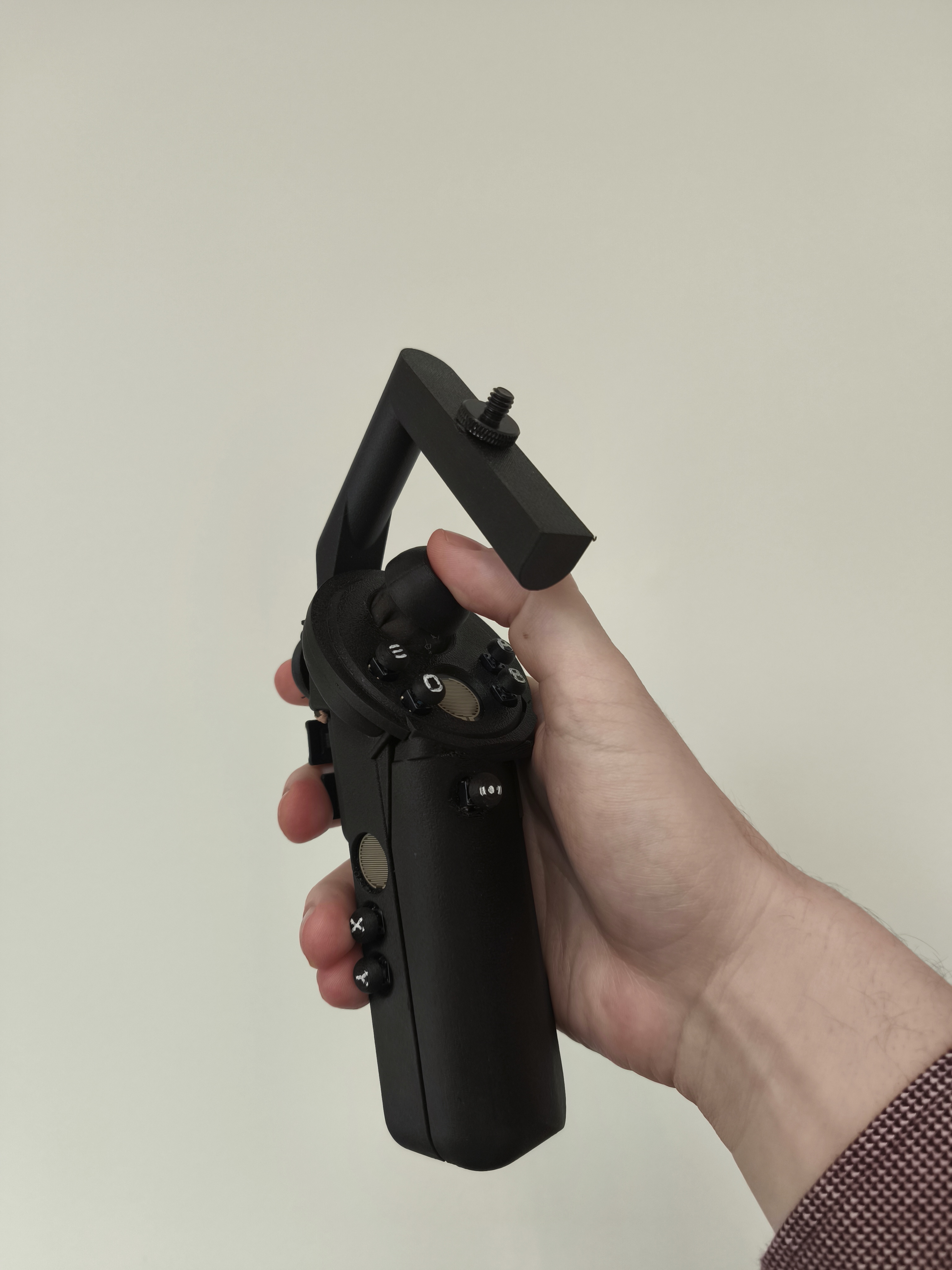 A black controller with buttons and joysticks is held in front of the camera. 