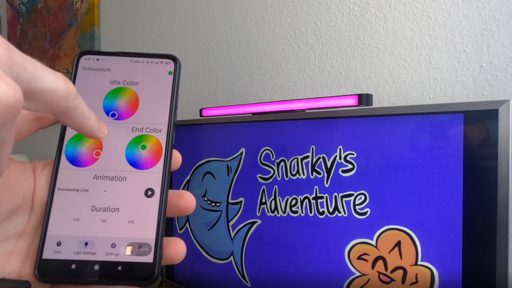 Snapshot of the "Schlusslicht" interface on a phone next to the lamp which is attached on a screen with a video game for kids.
